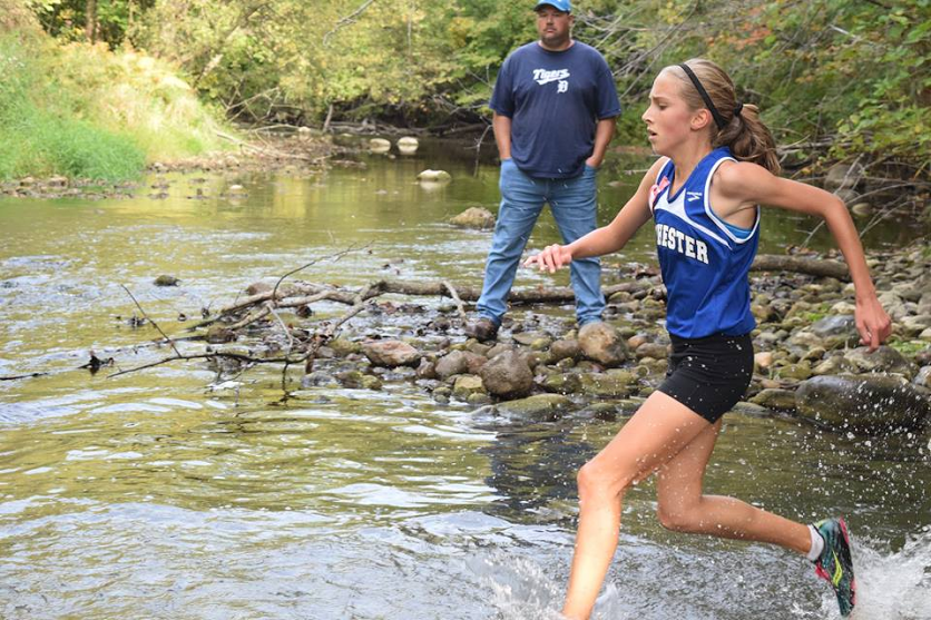 Freshman Elizabeth Bulat charges through the river at the Old Skool Classic cross country meet.